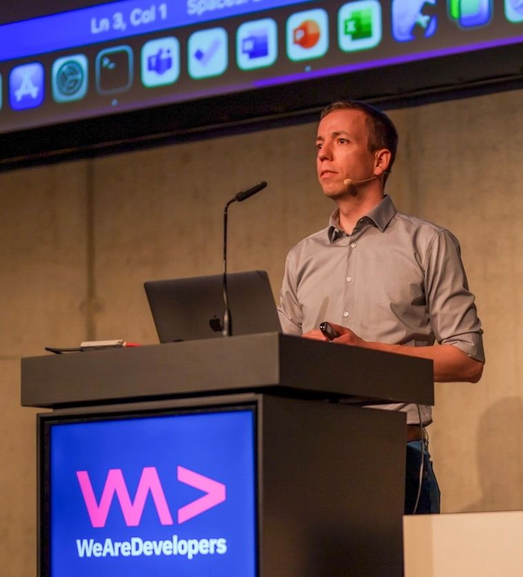 Christoph Menzel speaking at a conference, standing at a podium with a microphone and laptop